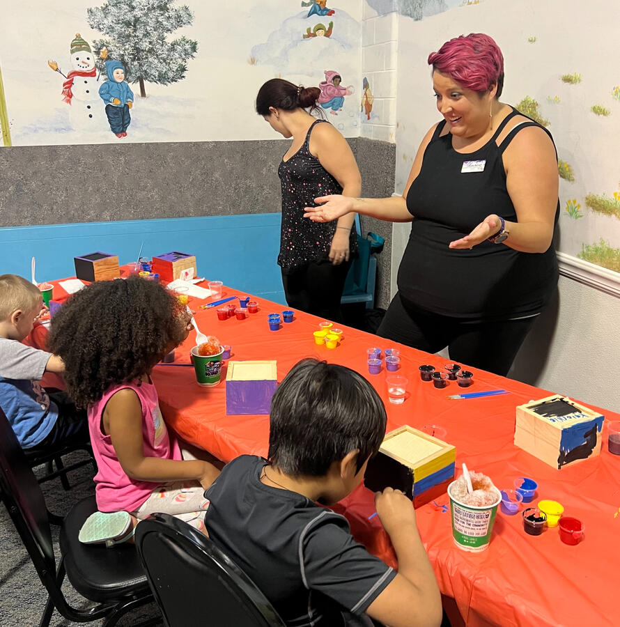 An art teacher at YWCA Dayton teaching a group of young children making art at a craft table